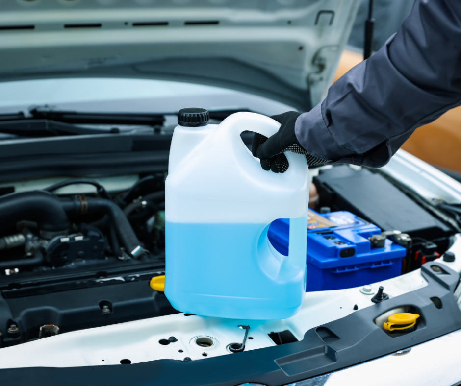 persona amb guants sostenint un bidó amb líquid anticongelant o refrigerant) dins del compartiment del motor d’un cotxe amb el capó obert